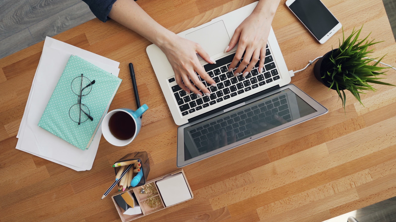 A person typing on a laptop at a wooden table, representing the writing and follow-up work behind outreach email templates